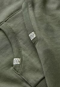 Olive green sweatshirt z materiału z ściągaczami na rękawach i kołnierzu. Zawiera metki z logo "Superdry". Strukturalna powierzchnia, swobodny design.