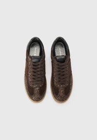 Sneaker in suede marrone con accenti luccicanti, rifiniture in pelle nera e lacci. Presenta una suola testurizzata e un design a punta arrotondata.