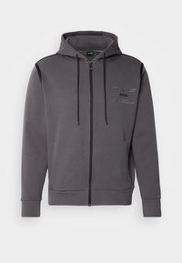 Felpa grigia con zip, cappuccio con coulisse, tasche laterali e dettagli neri. Presenta un logo sottile e una texture morbida in misto cotone.