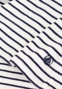 Camicia di cotone con righe orizzontali blu navy e bianche, con un polsino ripiegato e una piccola accentuazione con logo vicino all'orlo. Texture liscia.