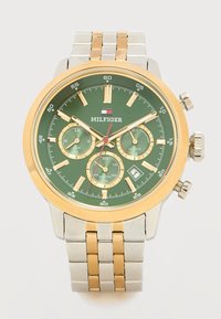 Ανδρικό ρολόι χειρός με πράσινο καντράν, χρυσή και ασημένια μεταλλική μπάντα, τρεις υποκαντράν, παράθυρο ημερομηνίας και χρυσή στεφάνη. Όνομα εμπορικής μάρκας κάτω από τον αριθμό 12.