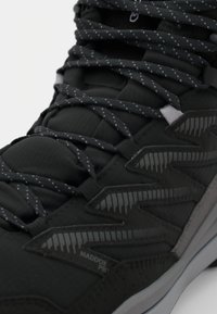 Pantof black sportiv cu partea superioară texturată, accente reflective și șireturi gri. Prezintă elemente de design în zigzag și un guler căptușit.