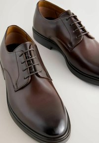 Braune Leder-Oxfords mit glatter Oberfläche, runder Zehenpartie, sechs Ösen Schnürdesign und einer niedrigen schwarzen Gummisohle.