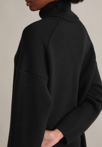 Schwarzer gestrickter Rollkragenpullover mit gerippten Bündchen und Kragen, der eine lockere Passform und glatte Textur bietet. Einfaches und modernes Design.