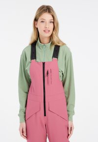 Roze overall met zwarte bandjes, rits aan de voorkant en zakken; gecombineerd met een lichtgroene geribbelde ritsjack. Eenvoudig en functioneel ontwerp.