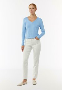 Helles blaues, langärmliges V-Ausschnitt-Sweatshirt, kombiniert mit weißen, schmal geschnittenen Hosen und beigen Slippern. Das Outfit zeichnet sich durch eine glatte Textur und ein minimalistisches Design aus.