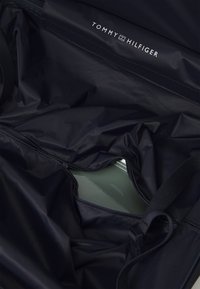 Interiore di un borsa in nylon nero con logo del marchio, caratterizzato da una base verde liscia. Include cerniere e cinturini per l'organizzazione e la chiusura.