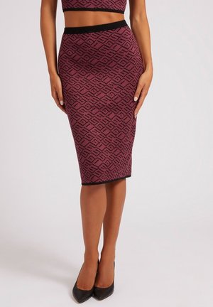 Femme portant une jupe crayon bordeaux ajustée mi-genou avec des motifs géométriques noirs et une ceinture noire, associée à des talons pointus noirs.