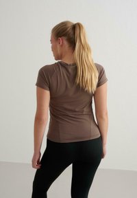 Braunes, tailliertes T-Shirt mit kurzen Ärmeln, glatter Textur und rundem Ausschnitt, kombiniert mit schwarzen Leggings. Die Rückansicht zeigt die Schlichtheit des Designs.
