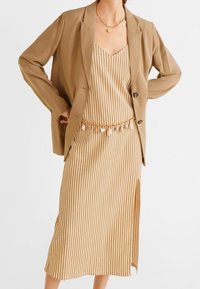 Beige stribede midi kjole med sideslids, lagd under en løs tanfarvet blazer, accessorized med et guld kæde bælte og halskæde.