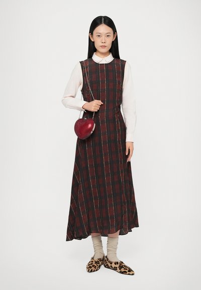 Abito midi a quadri in rosso scuro e nero con una camicia bianca con colletto sotto; borsa a forma di cuore rossa e pantofole con stampa leopardata.