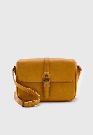 Sac bandoulière jaune moutarde avec fermeture à boucle à l'avant et bandoulière ajustable sur fond gris clair.