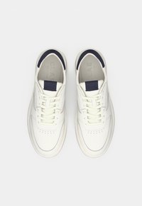 White leather sneakers with navy accents on the tongue and heel, featuring laces and perforated details, viewed from above on a white background.
