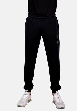Pantaloni jogging neri in fleece con vita elasticizzata, caviglie affusolate e tasche laterali. Abbinati a sneakers sportive bianche con dettagli in rete.