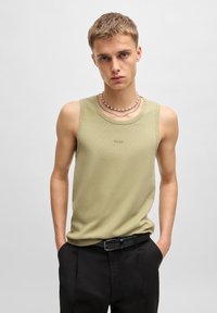 Débardeur sans manches couleur kaki avec une texture c�ôtelée et un branding subtil. Associé à un pantalon noir et des colliers à perles superposés.