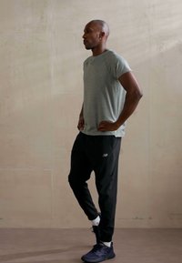 Sportoutfit bestehend aus einem grauen T-Shirt mit kurzen Ärmeln, schwarzen Jogginghosen mit Logo und dunklen Sneakers. Glatter Stoff und figurbetontes Design.