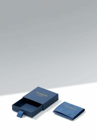 Två blå smyckesbehållare från Su Jacobs, en öppen med en del av lådan utdragen och en stängd påse, på en vit yta.