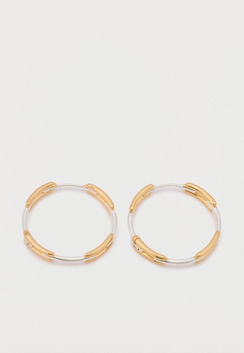 Auksiniai ir sidabriniai žiedai auskariuose su lanksčiu dizainu, auksiniais akcentais ir lygiomis tekstūromis, apjungiantys minimalistinį, modernų stilių.