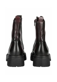 Botas de tobillo de cuero marrón con un acabado suave, punteras redondeadas y suelas de goma negra gruesa. Cuentan con cremalleras laterales para una fácil puesta.