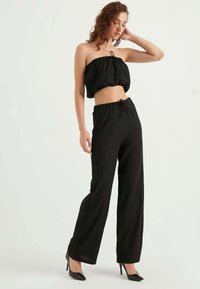 Black cropped strapless top with gathered texture, paired with high-waisted black wide-leg pants featuring a drawstring waist.