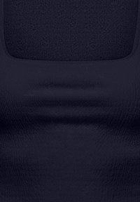 Gros plan sur un tissu noir avec un col carré et une texture subtile, montrant de légères plis et des détails de couture.
