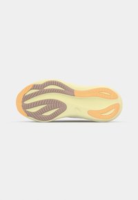 Semelle de chaussure avec un motif ondulé dans des sections en caoutchouc beige, marron et orange sur une base jaune clair, affichée sur un fond gris.