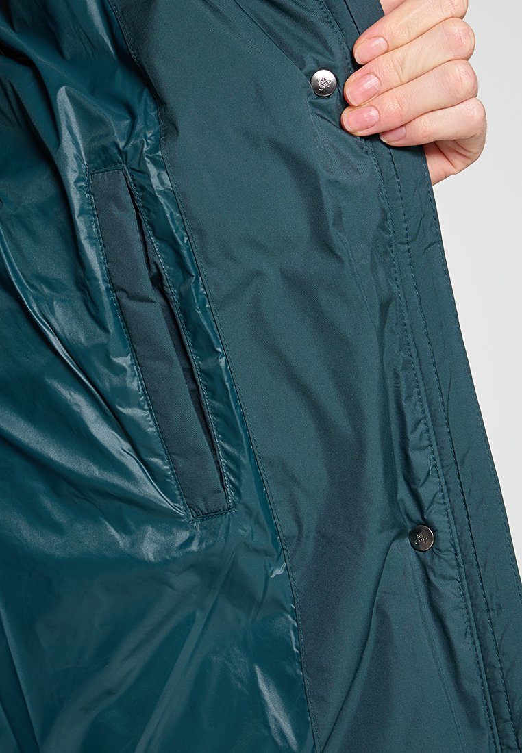 Türkise, leichte Jacke mit glatter Textur, ausgestattet mit einem Druckknopfverschluss und seitlicher Tasche. Das Innere verfügt über ein dunkleres Stofffutter.