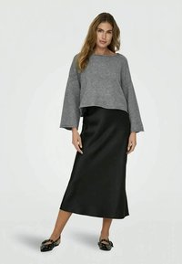 Suéter cinza curto com mangas largas, combinado com uma saia maxi preta de cetim e sapatos pretos de deslizar com laços. Texturas suaves e design minimalista.