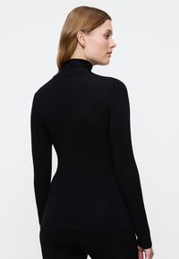 Maglietta nera a collo alto con maniche lunghe, design aderente, realizzata in tessuto morbido. La vista posteriore mostra una silhouette pulita e cuciture minime.