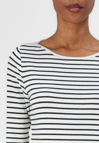 Chemise à manches longues avec des rayures horizontales bleu marine et blanches, texture côtelée et encolure ronde. Le tissu semble doux et extensible.
