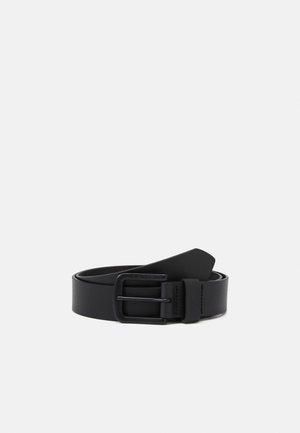 Ceinture en cuir noir enroulée avec une boucle rectangulaire en métal noir mat, sur un fond clair uni.