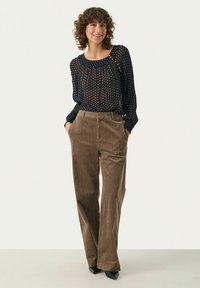 Marineblauwe doorzichtige blouse met polka dots, lange mouwen en ronde hals, gecombineerd met hoge taille, brede bruine corduroy broek. Zwarte hakken.
