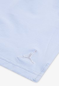 Světlomodrá tkanina s hladkým povrchem, na rohu s bílou vyšívanou logem Jumpman. Rovný lem s čistým švem.