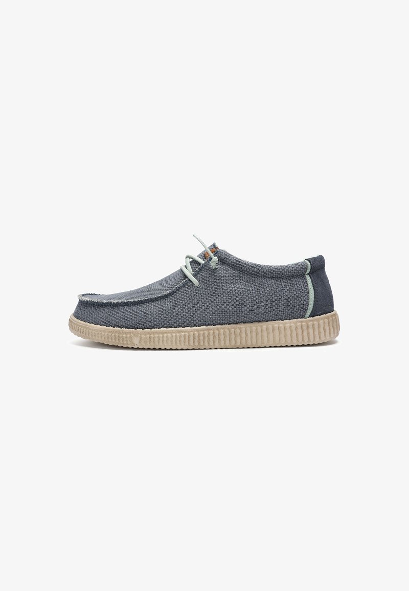 Chaussure décontractée basse avec tissu texturé bleu marine, semelle en caoutchouc beige, lacets gris clair et détails de couture minimaux, vue de profil latéral.