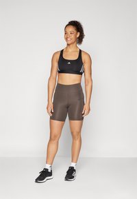 Svart sportsbh med hvite aksentstriper, brune tettsittende shorts og svarte treningssko. Glatt stoff og høy midje for komfort.