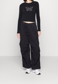 Černý dlouhý rukáv zkrácený top s motivem motýla, spárovaný s volnými černými cargo kalhotami. Tenisky doplňují celý outfit.