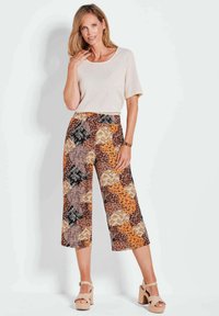 Beige gebreid topje met korte mouwen, gecombineerd met wijde broek met oranje, bruin en zwarte bloemen- en geometrische patronen. Chunky heeled sandalen.