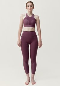 Lila sportbh med hög halsringning och strukturerade sömmar, kombinerad med matchande högmidjade leggings med subtila accenter och en mjuk textur.