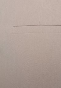 Lichtbeige stof, gladde textuur, met een enkele achterzak met een rechte opening en subtiele stikaccenten.