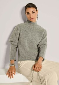 Hellgrauer, gestrickter Pullover mit hohem Kragen, lockerer Passform und gerippter Textur; kombiniert mit cremefarbener, gerippter Hose. Einfaches und modernes Design.