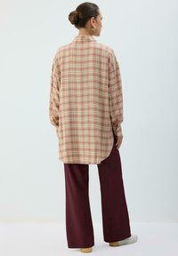 Chemise longue à carreaux pastel rose et jaune, associée à un pantalon burgundy à jambes larges. Tissu léger avec une coupe décontractée et un ourlet arrondi.