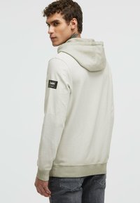 Light grey hoodie with a contrast hood, ribbed cuffs, and hem. Features a black label on the left sleeve. Simple, casual design.