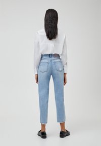 Lichtblauwe denim jeans met een hoge taille, korte lengte en rafelige zomen. Gecombineerd met een wit shirt met een geplooide achterkant.