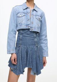 Ljusblå denimjacka i kort modell med knäppning och två framfickor, tillsammans med en rynkad denimklänning med utsvängd kjol.