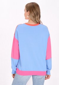 Felpa color block con sezioni blu chiaro e rosa, colletto rotondo e maniche lunghe. Tessuto testurizzato con polsini a costine.