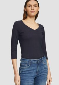 Zwarte lange mouwen V-hals top gecombineerd met blauwe jeans. De top heeft een aangesloten ontwerp en ribbeltextuur, geschikt voor casual draagstijl.