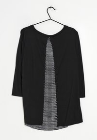 Maglietta nera a maniche lunghe con un pannello a contrasto con motivo a nido d'ape bianco, in tessuto liscio, e orlo curvo. Appesa a un gancio nero.