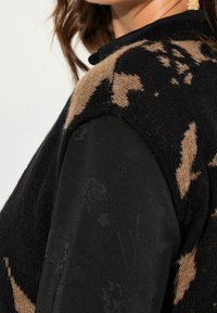 Schwarzer und tanfarbener Strickpullover mit einer fusseligen Textur, der ein florales Muster im tanfarbenen Bereich und einen glatten schwarzen Ärmel hat.