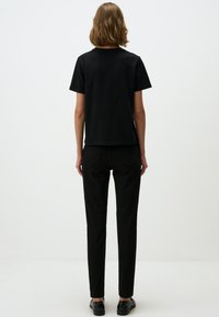 Zwart T-shirt met korte mouwen en een rechte snit, gecombineerd met zwarte slim-fit jeans. De outfit heeft een eenvoudige textuur en een minimalistisch ontwerp.