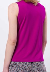 Persona con top magenta senza maniche e gonna a fantasia multicolore, vista da dietro su uno sfondo bianco.